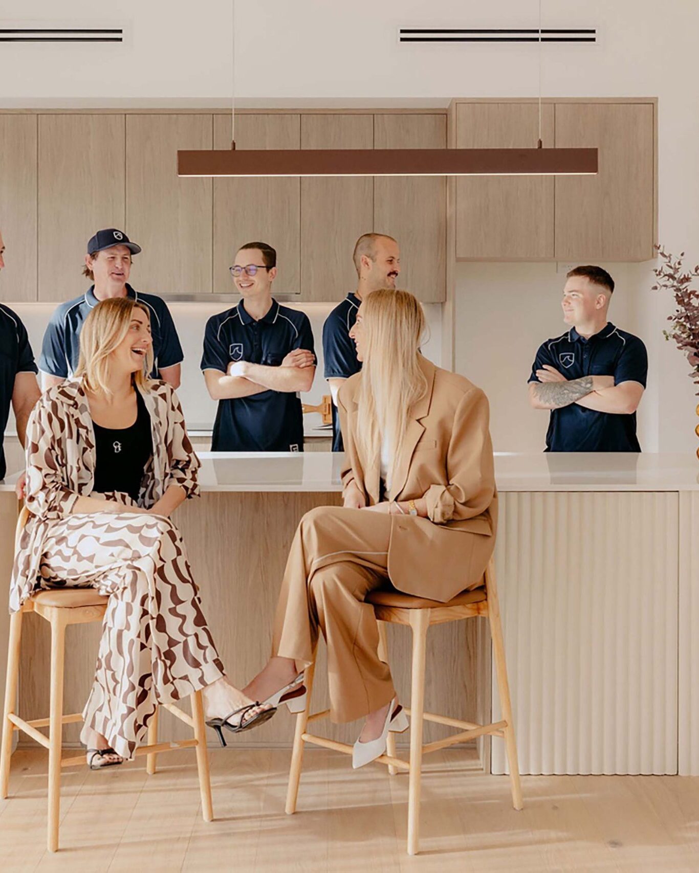 Indianic Homes team gathered in contemporary kitchen with timber cabinetry and curved island bench