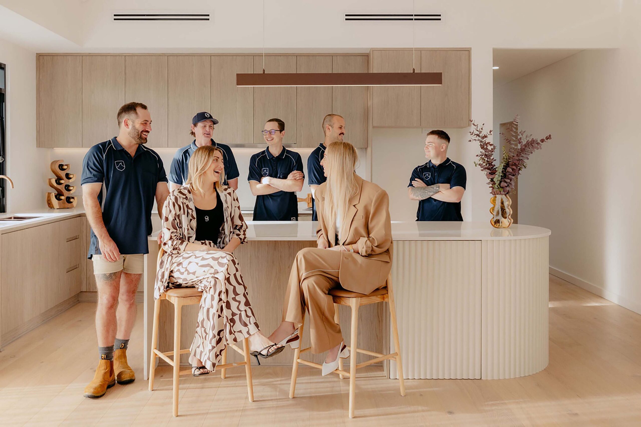 Indianic Homes team gathered in contemporary kitchen with timber cabinetry and curved island bench