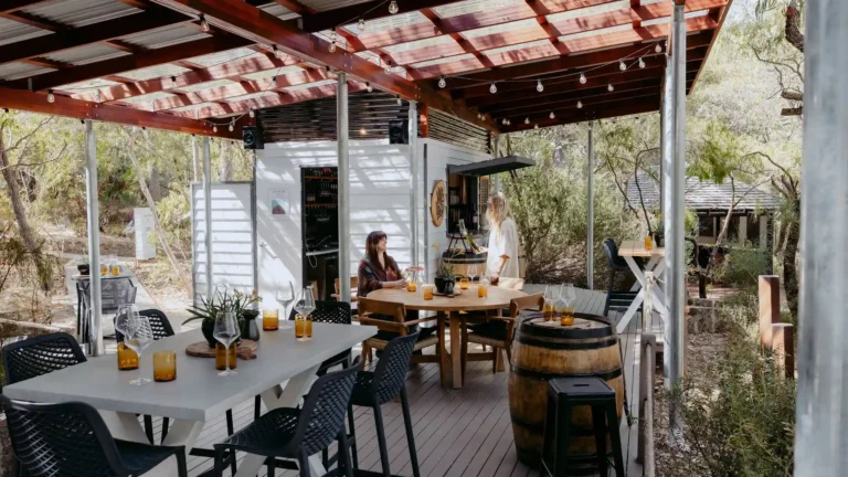 Two guests enjoying a wine tasting experience at Valle du Venom cellar door in Yallingup, seated on the covered deck surrounded by native bushland